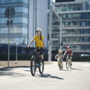 Aikuinen pyöräilee pyörätiellä kahden lapsen kanssa. Kaikilla on kypärät päässä.