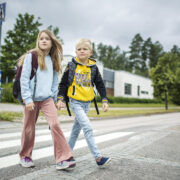 Kaksi lasta ylittää suojatien käsi kädessä.