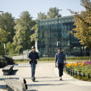 Sähköpotkulaudalla kulkeva henkilö sekä jalankulkija rinnakkain yhdistetyllä jalankulku- ja pyörätiellä.
