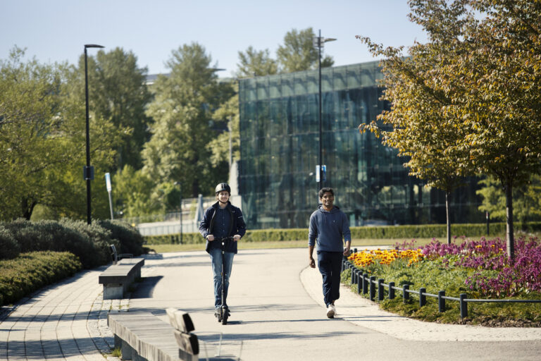 Sähköpotkulaudalla kulkeva henkilö sekä jalankulkija rinnakkain yhdistetyllä jalankulku- ja pyörätiellä.