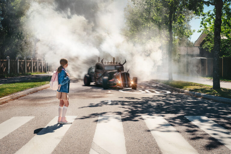 Tyttö kävelee suojatiellä. Savuttava hirviöauto lähestyy suojatietä.
