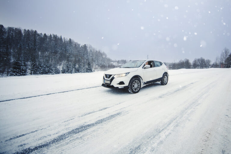 Auto ajaa lumisella tiellä.