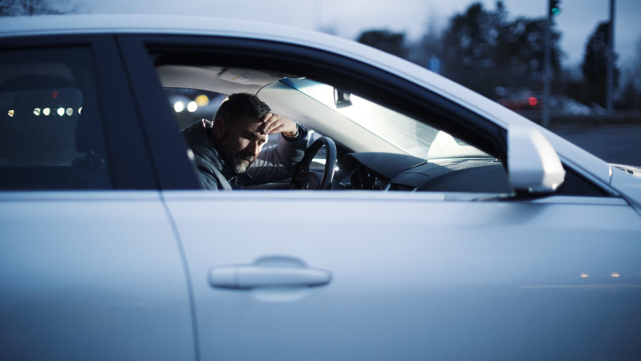 Kuljettaja nojaa pysäköidyssä autossa rattiin.