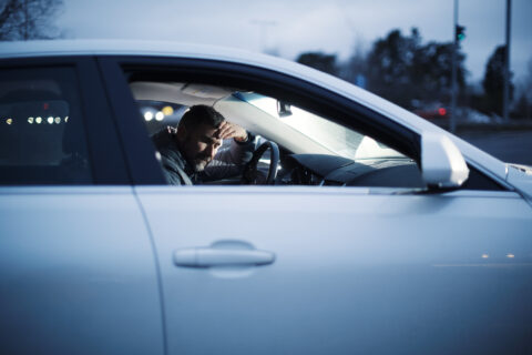 Kuljettaja nojaa pysäköidyssä autossa rattiin.