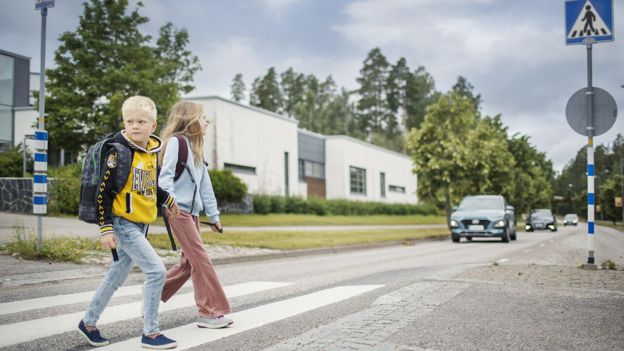 Lapset kävelevät suojatiellä matkalla kouluun ja auto on pysähtynyt kauempana.