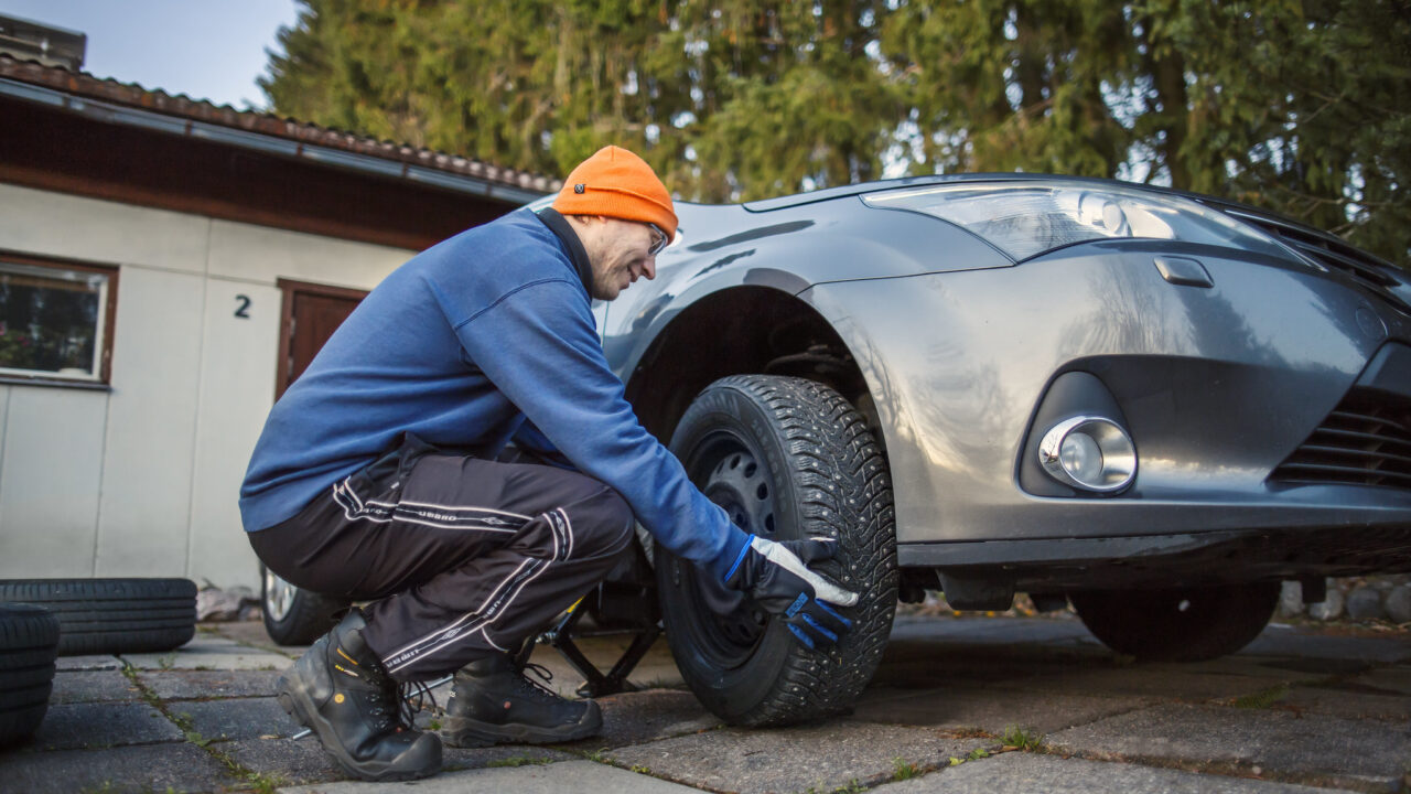 Autoilija vaihtaa talvirenkaita autoonsa.