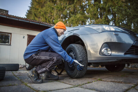 Autoilija vaihtaa talvirenkaita autoonsa.