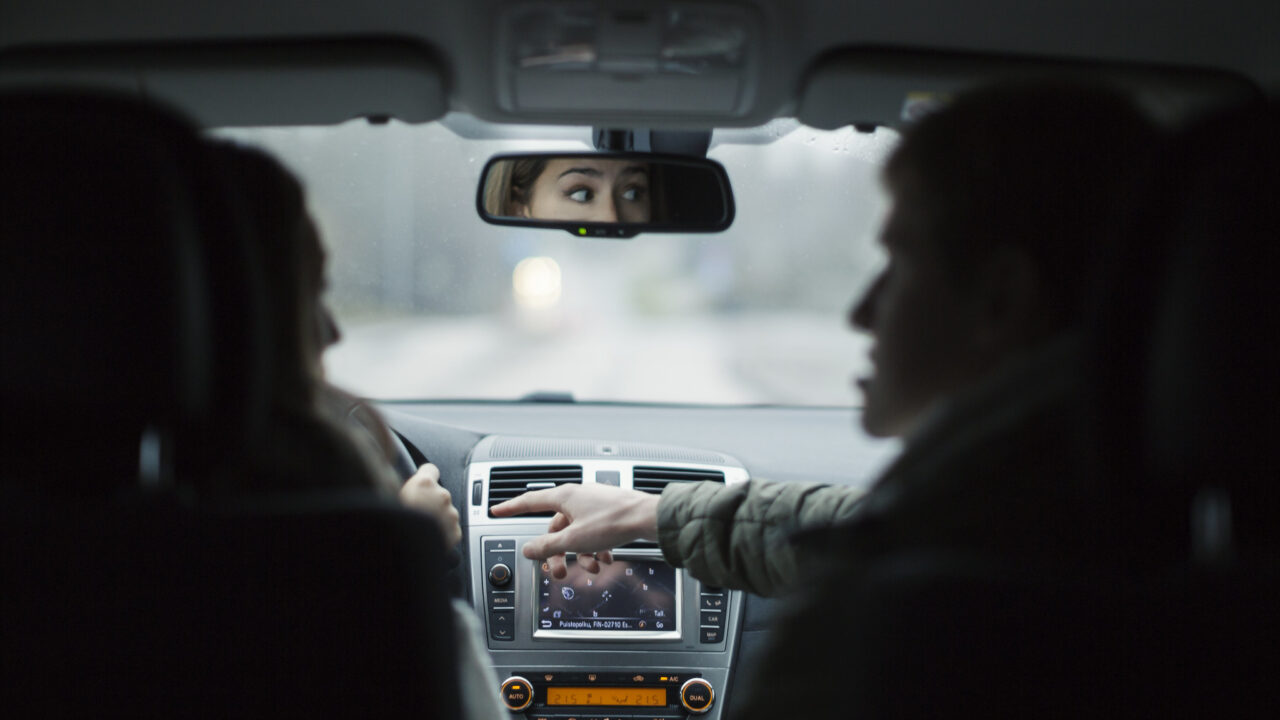 Etupenkin matkustaja osoittaa kojetaulua kuljettajalle.