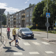 Pyöräilijä ja auto pysähtyneenä suojatien eteen, jota pitkin kävelee kaksi jalankulkijaa