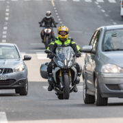 Moottoripyöräilijä matkustajineen vilkkaassa liikenteessä.