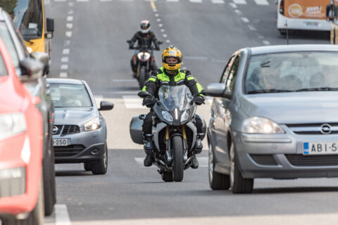 Moottoripyöräilijä matkustajineen vilkkaassa liikenteessä.